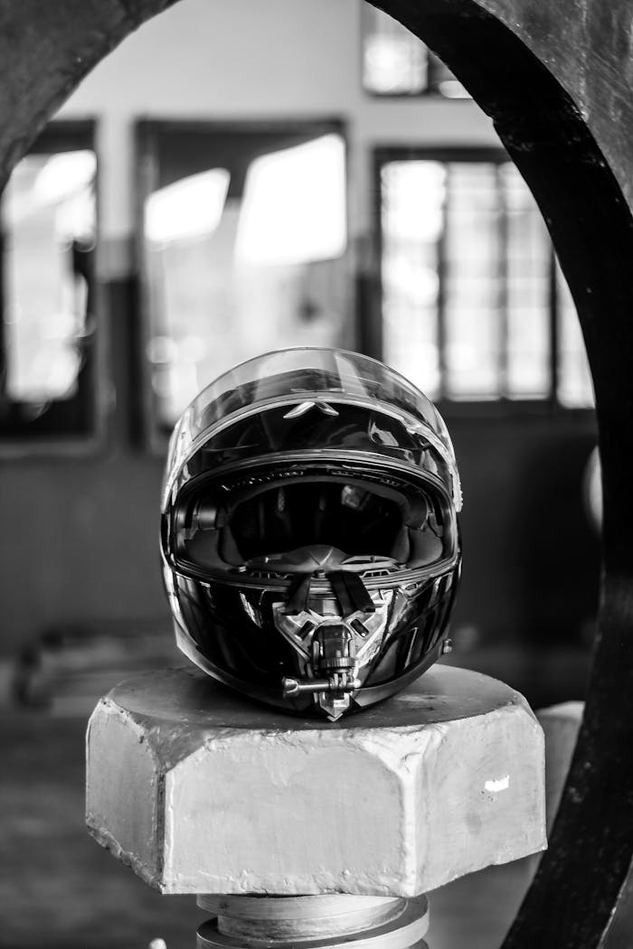 Monochrome image of a helmet displayed on a pedestal, framed by industrial elements in a workshop.
