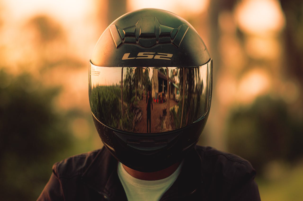 Close-up of a motorcyclist wearing a reflective helmet, capturing outdoor reflections during sunset.